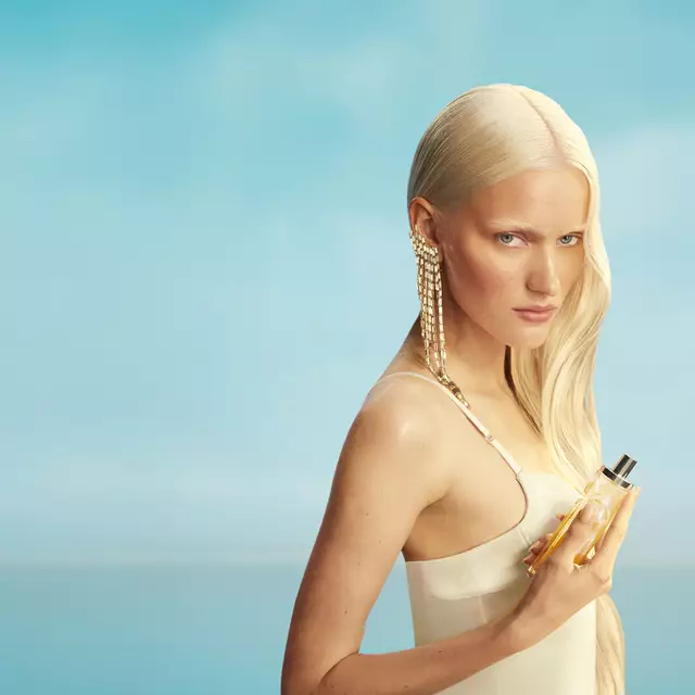 Nouvelle bannière de campagne Mugler Starlicious les eaux gourmandes représentant un mannequin aux longs cheveux blonds et aux yeux bleus, portant une robe jaune pâle et tenant le flacon de parfum Pineapple Musk sur un fond de ciel bleu tendre. Les parfums sont délicieux, à collectionner et à superposer.