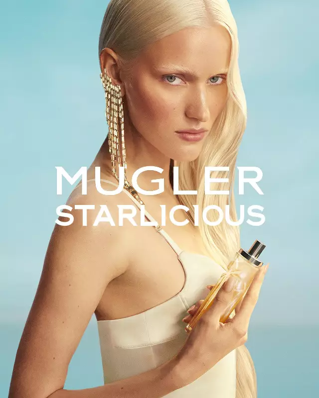 Bannière de campagne Mugler Starlicious Les Eaux Gourmandes avec le modèle en robe jaune pâle tenant le flacon Pineapple Musk sur fond de ciel bleu tendre.